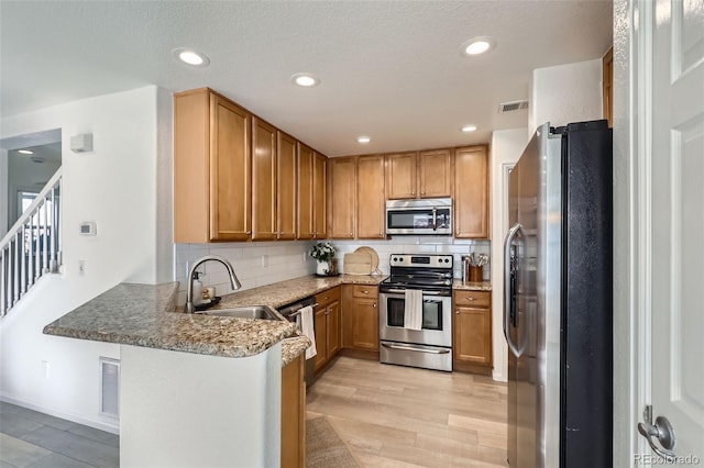 kitchen featuring kitchen peninsula, sink, light wood-type flooring, appliances with stainless steel finishes, and light stone counters