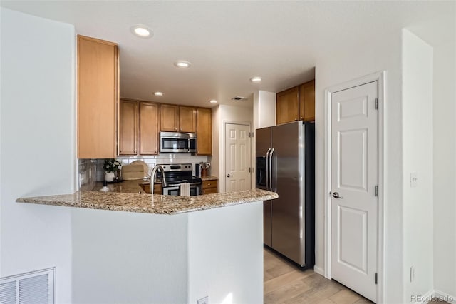 kitchen with light hardwood / wood-style floors, kitchen peninsula, appliances with stainless steel finishes, backsplash, and light stone countertops