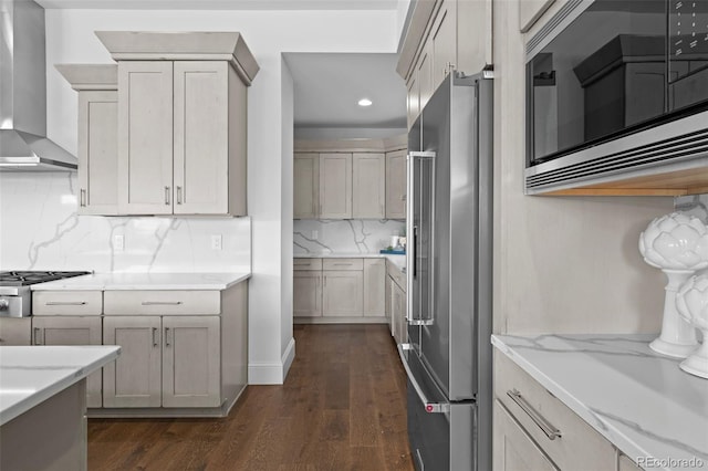 kitchen featuring backsplash, stainless steel appliances, light stone countertops, dark hardwood / wood-style flooring, and wall chimney exhaust hood