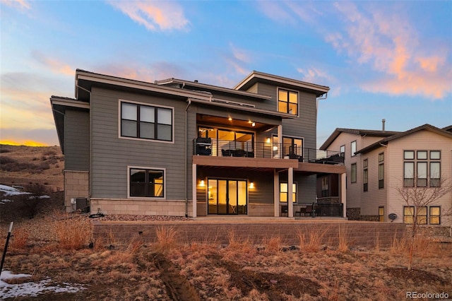 back house at dusk featuring a patio, a balcony, and central air condition unit