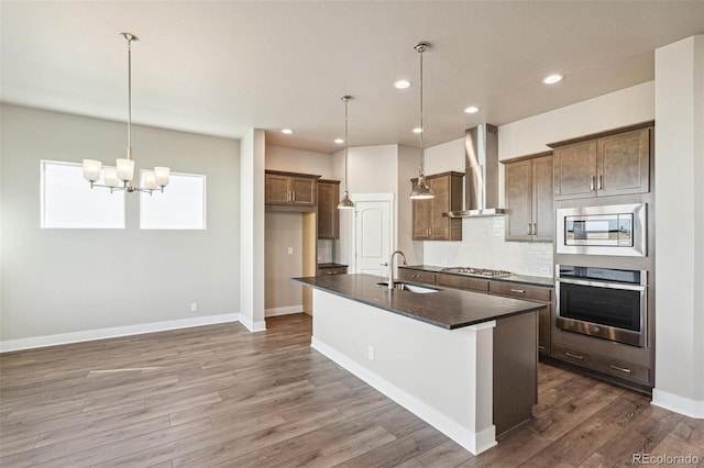 21295 E 61st Dr, Aurora, CO 80019 - kitchen featuring dark countertops, wall chimney exhaust hood, a kitchen island with sink, appliances with stainless steel finishes, and dark wood-style flooring