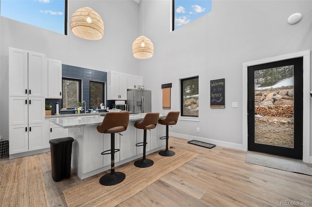 379 Rainbow Rd, Idaho Springs, CO 80452 - kitchen with stainless steel fridge with ice dispenser, a towering ceiling, a breakfast bar, white cabinets, and light wood finished floors