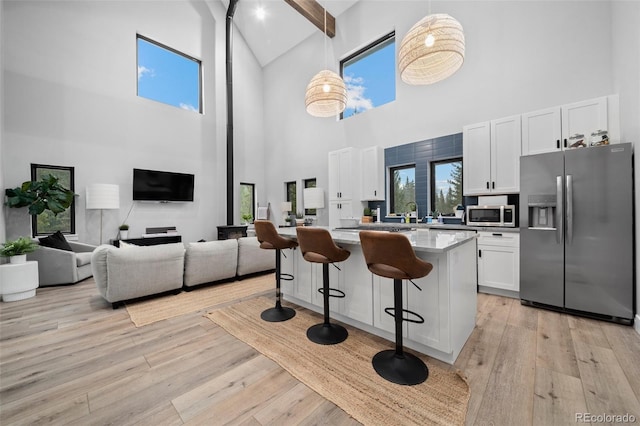 379 Rainbow Rd, Idaho Springs, CO 80452 - kitchen featuring appliances with stainless steel finishes, high vaulted ceiling, a kitchen bar, white cabinetry, and light wood-style floors