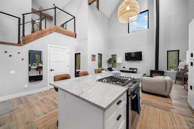 379 Rainbow Rd, Idaho Springs, CO 80452 - kitchen featuring gas range, high vaulted ceiling, a wood stove, white cabinets, and light wood finished floors