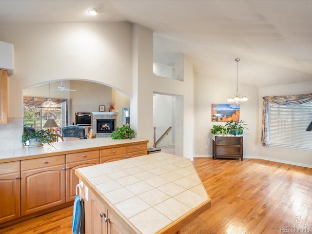7158 W Belmont Dr, Littleton, CO 80123 - kitchen featuring tile countertops, hanging light fixtures, a fireplace, vaulted ceiling, and light wood-style floors
