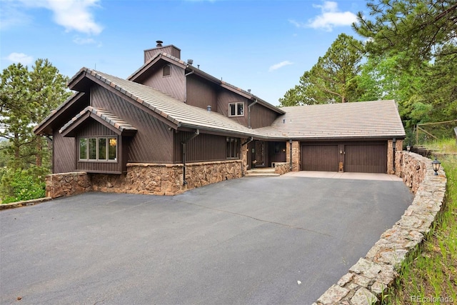 2851 Interlocken Dr, Evergreen, CO 80439 - chalet / cabin featuring an attached garage, asphalt driveway, a chimney, and stone siding