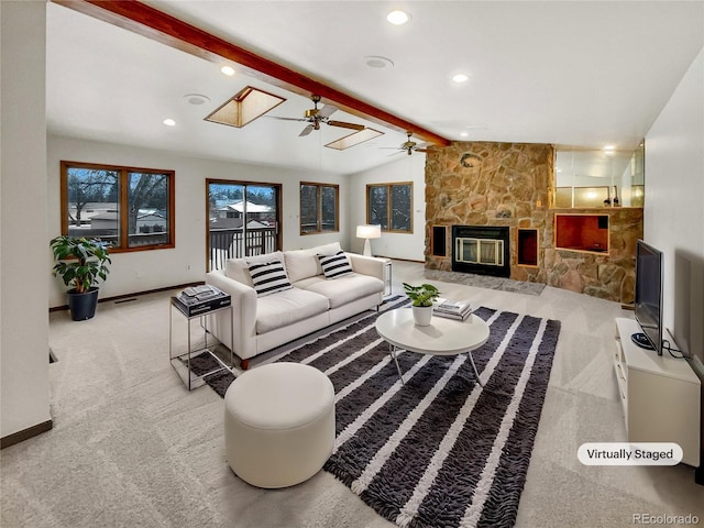 carpeted living area with vaulted ceiling with skylight, baseboards, visible vents, a fireplace, and recessed lighting