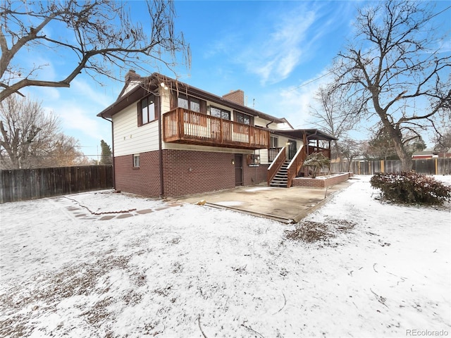 snow covered property with a deck, a fenced backyard, brick siding, stairs, and a patio area