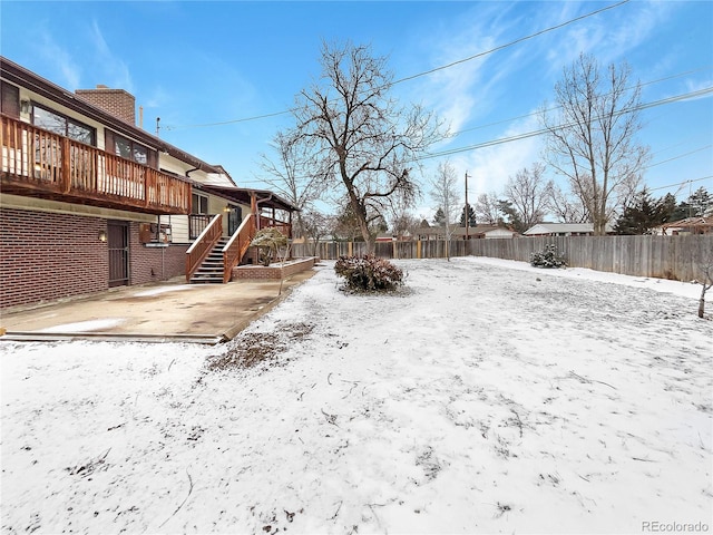 snowy yard with a fenced backyard, stairs, a patio, and a wooden deck