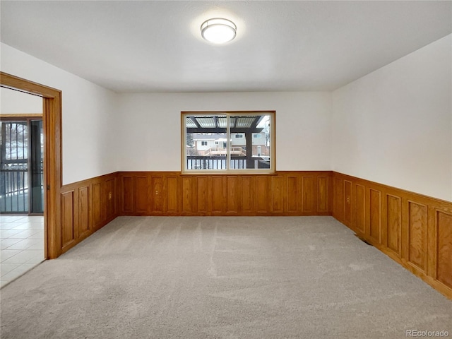 spare room featuring a wainscoted wall, light tile patterned flooring, and light colored carpet