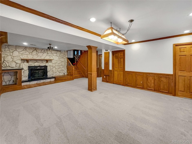 unfurnished living room featuring crown molding, stairway, a stone fireplace, and wainscoting