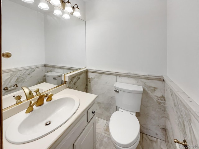 half bathroom with wainscoting, toilet, marble finish floor, vanity, and a notable chandelier