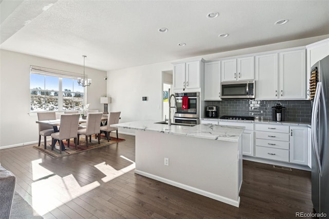 kitchen featuring pendant lighting, stainless steel appliances, an island with sink, and white cabinets