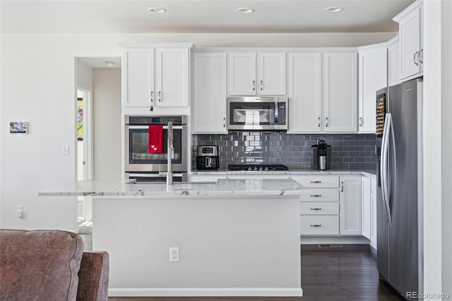 kitchen featuring white cabinetry, stainless steel appliances, dark hardwood / wood-style floors, light stone counters, and an island with sink