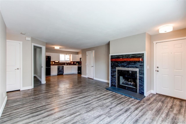 unfurnished living room with dark wood finished floors, baseboards, a fireplace with raised hearth, and a sink
