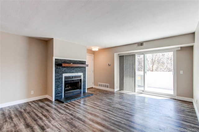 unfurnished living room featuring dark wood-type flooring, a stone fireplace, and baseboards