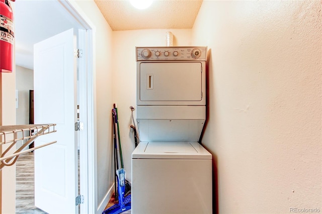 clothes washing area with stacked washing machine and dryer and wood finished floors