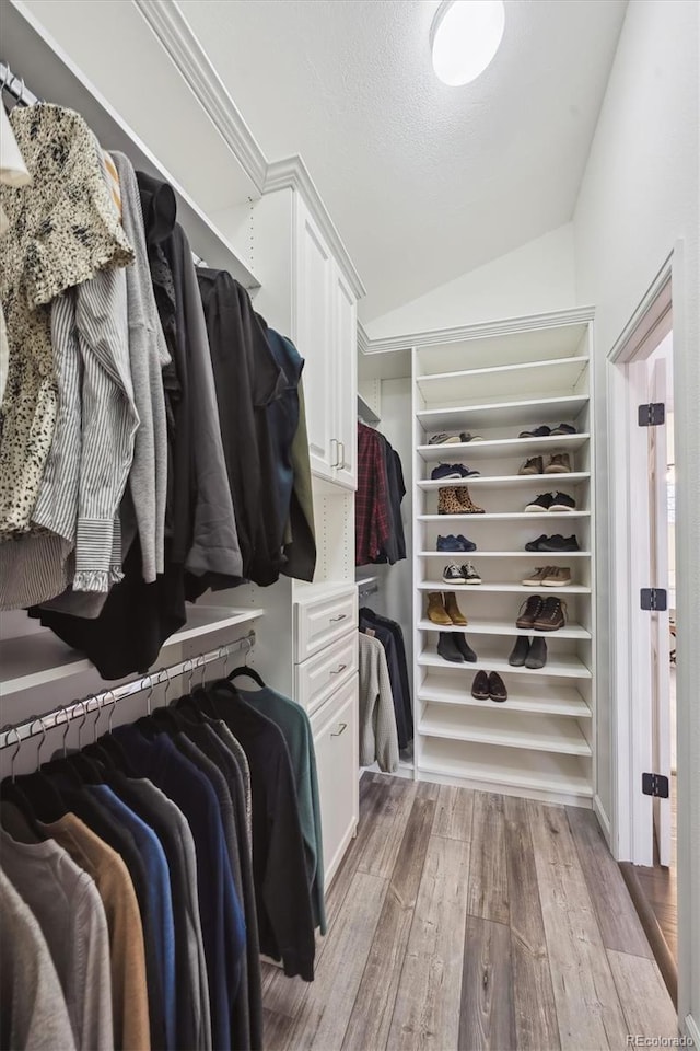 spacious closet with light hardwood / wood-style floors and lofted ceiling