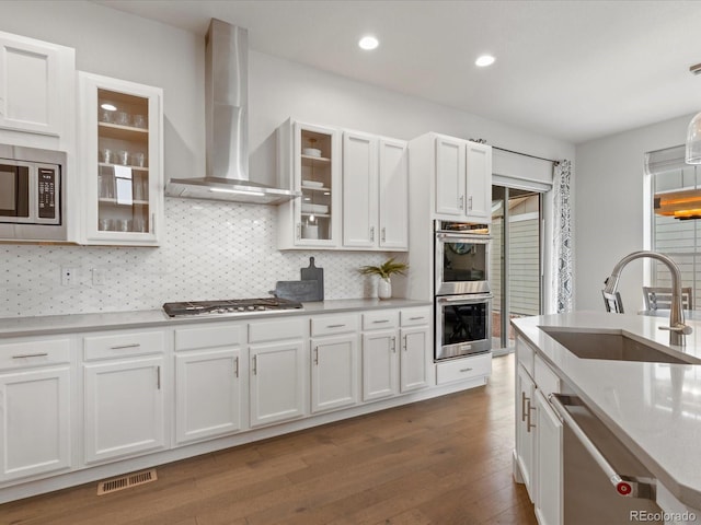 kitchen with appliances with stainless steel finishes, a sink, wall chimney exhaust hood, white cabinetry, and visible vents