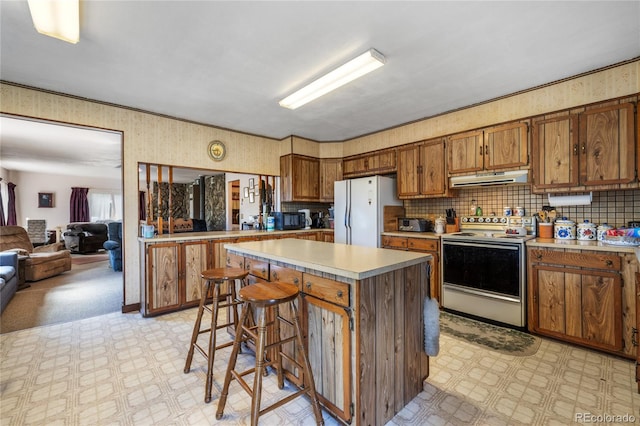 kitchen featuring a kitchen island, a breakfast bar, white appliances, and decorative backsplash