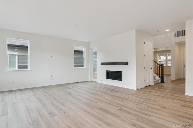8205 Cokedale Cir, Littleton, CO 80125 - unfurnished living room with light wood-type flooring, stairs, a glass covered fireplace, baseboards, and recessed lighting