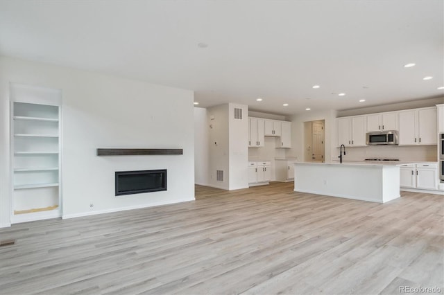 8205 Cokedale Cir, Littleton, CO 80125 - unfurnished living room with recessed lighting, a glass covered fireplace, light wood-type flooring, a sink, and baseboards