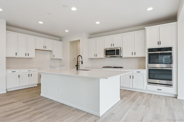 8205 Cokedale Cir, Littleton, CO 80125 - kitchen featuring appliances with stainless steel finishes, a sink, light wood-style floors, a center island with sink, and recessed lighting