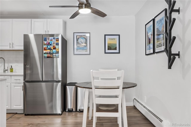 kitchen with white cabinetry, a baseboard radiator, stainless steel fridge, and decorative backsplash