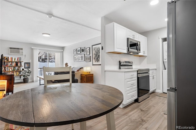 kitchen with light hardwood / wood-style flooring, a wall unit AC, stainless steel appliances, tasteful backsplash, and white cabinets