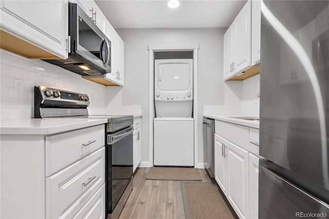 kitchen featuring stacked washer / drying machine, wood-type flooring, white cabinets, stainless steel appliances, and backsplash