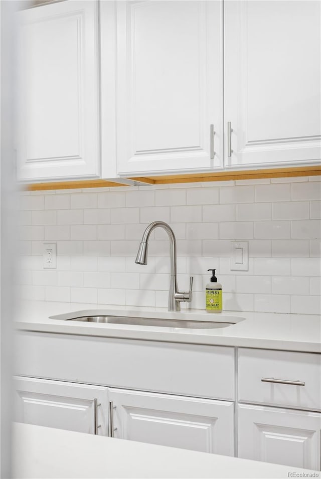 details with tasteful backsplash, white cabinetry, and sink