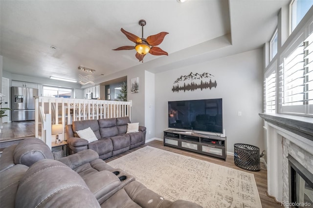 living room featuring ceiling fan, a stone fireplace, and light hardwood / wood-style floors