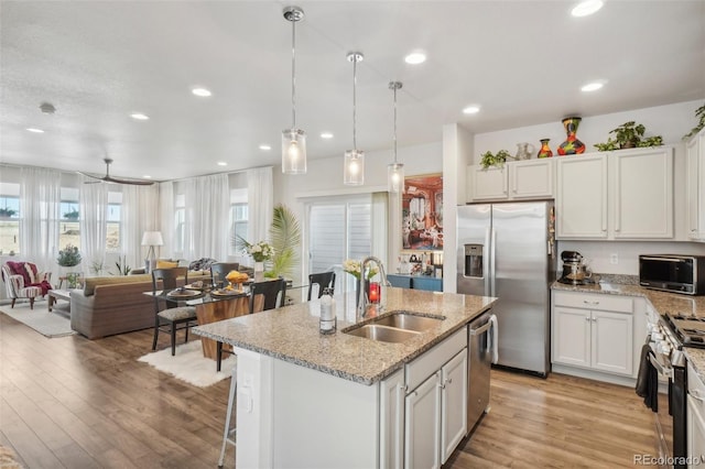 kitchen featuring pendant lighting, a kitchen island with sink, sink, appliances with stainless steel finishes, and light hardwood / wood-style floors