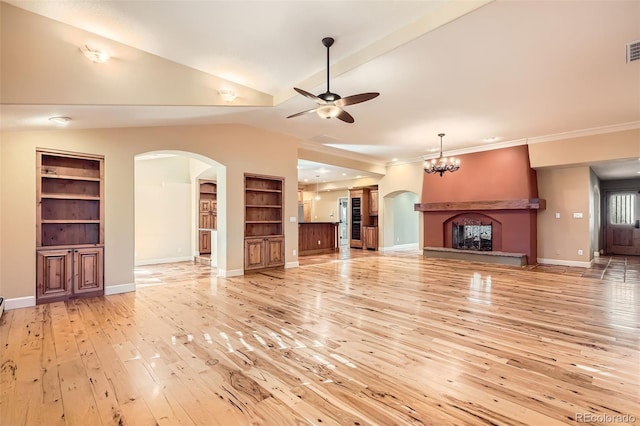 unfurnished living room with built in shelves, arched walkways, light wood-type flooring, and ceiling fan with notable chandelier