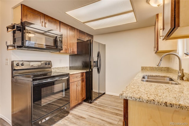 kitchen featuring light stone countertops, sink, light hardwood / wood-style flooring, and black appliances