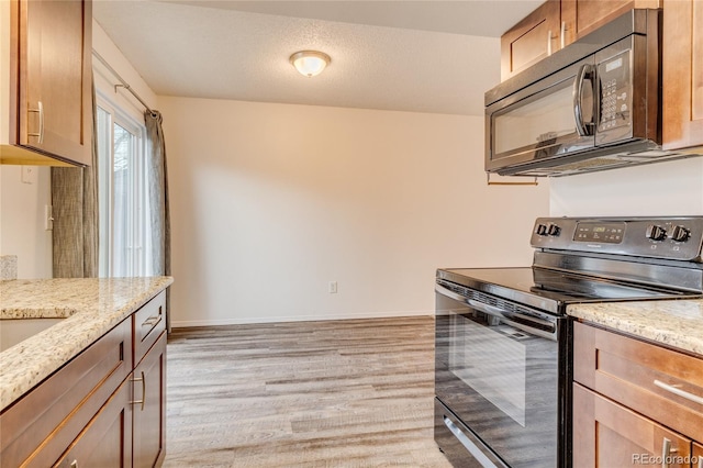 kitchen featuring light stone countertops, a textured ceiling, light wood-type flooring, and black appliances