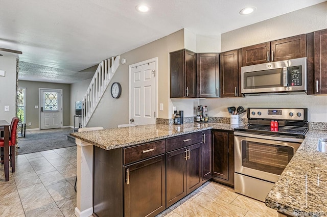 12059 E Hoye Dr, Aurora, CO 80012 - kitchen with appliances with stainless steel finishes, dark brown cabinetry, light stone countertops, a peninsula, and open floor plan