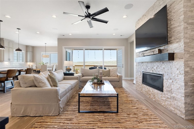 living room featuring ceiling fan, a stone fireplace, and light hardwood / wood-style floors