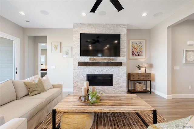 living room featuring ceiling fan, a stone fireplace, and light hardwood / wood-style flooring