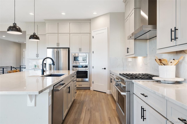 kitchen featuring wall chimney exhaust hood, a center island with sink, white cabinets, and appliances with stainless steel finishes