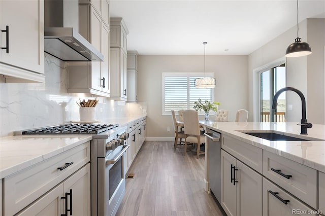 kitchen featuring wall chimney range hood, high end range, pendant lighting, sink, and decorative backsplash