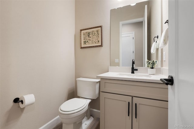 half bath featuring baseboards, vanity, and toilet