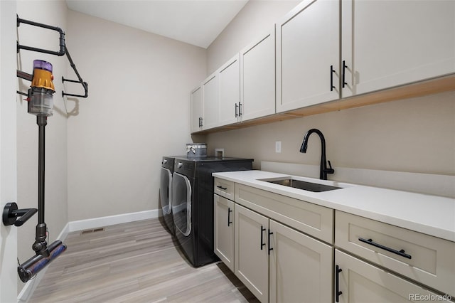 clothes washing area featuring cabinet space, baseboards, washer and clothes dryer, light wood-style flooring, and a sink