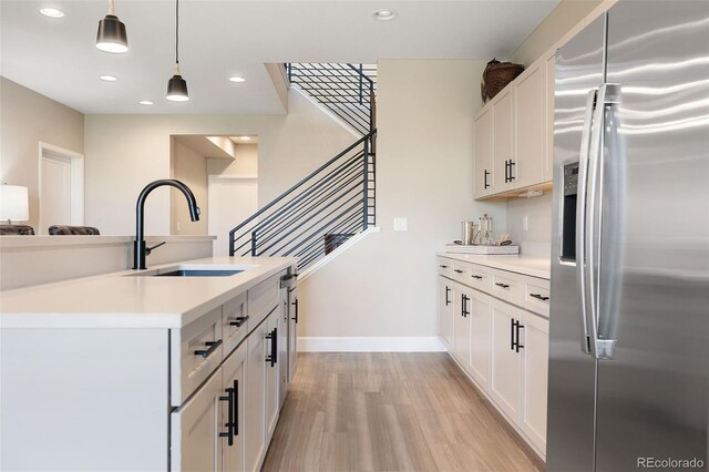 kitchen with pendant lighting, stainless steel appliances, light countertops, a sink, and light wood-type flooring