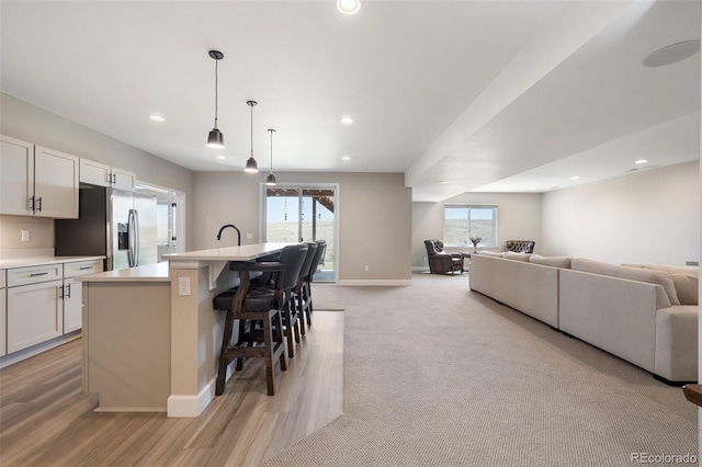 kitchen with stainless steel refrigerator with ice dispenser, a wealth of natural light, light countertops, open floor plan, and a kitchen breakfast bar