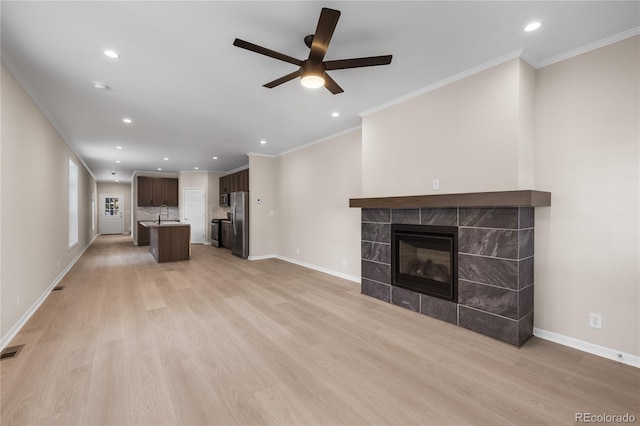 unfurnished living room featuring ceiling fan, a fireplace, sink, light wood-type flooring, and ornamental molding