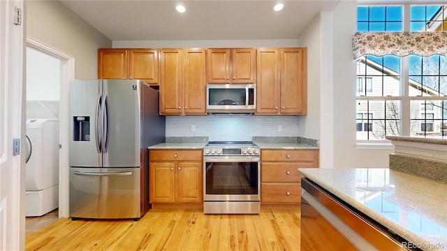 kitchen with light stone counters, stainless steel appliances, light wood-style floors, tasteful backsplash, and washer / dryer