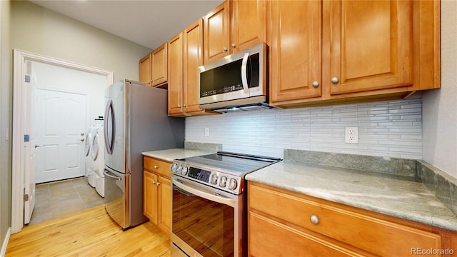 kitchen with light countertops, appliances with stainless steel finishes, washing machine and dryer, and tasteful backsplash