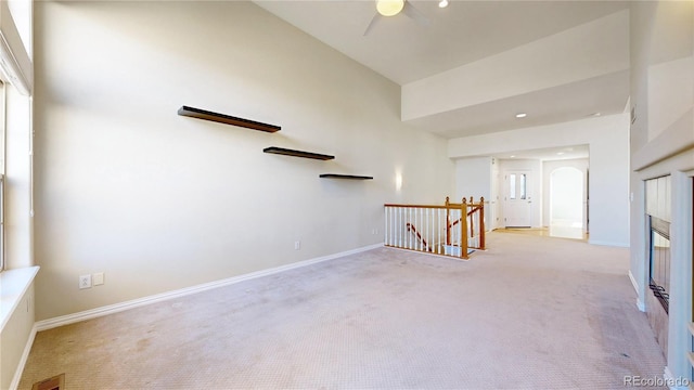 empty room with arched walkways, light carpet, visible vents, baseboards, and a glass covered fireplace