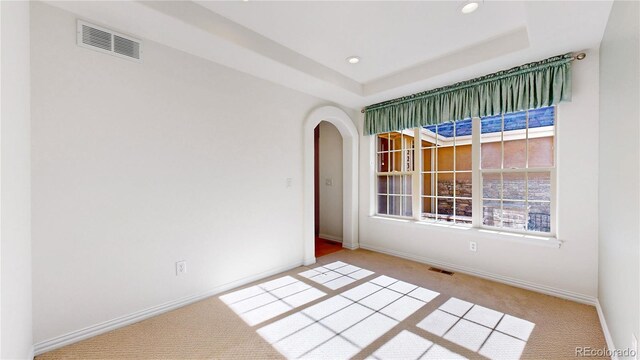 empty room featuring carpet, a raised ceiling, and visible vents